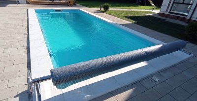 Прямоугольный композитный бассейн с защитным рулоном и светлой плиткой на улице